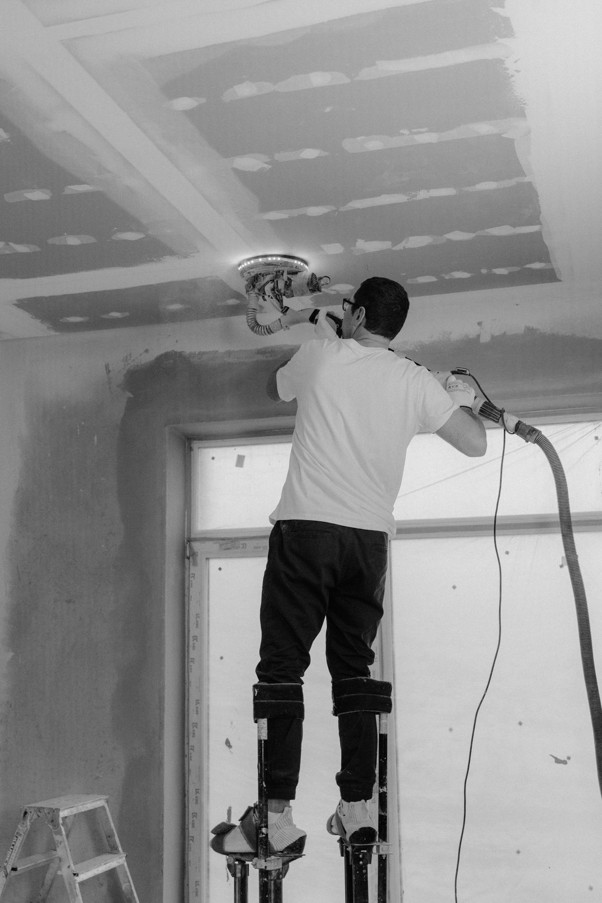 Tradesman on stilts running a sander across a freshly skim-coated ceiling