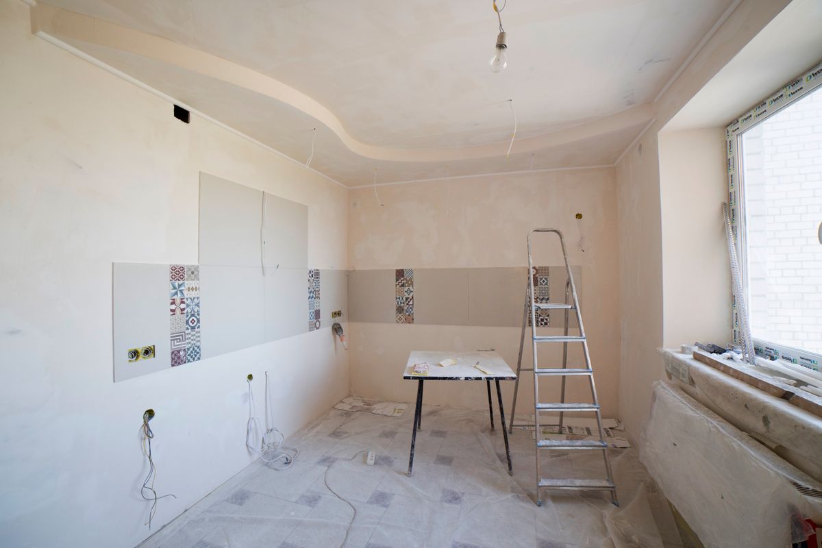 Room prepped for ceiling work with a stepladder, drop cloths, and masked surfaces